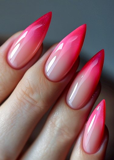 Stunning stiletto nails feature a gradient from nude to vibrant pink with sparkles.