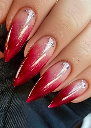 Stunning ombre red and nude stiletto nails with jewel embellishments for elegant nail art.