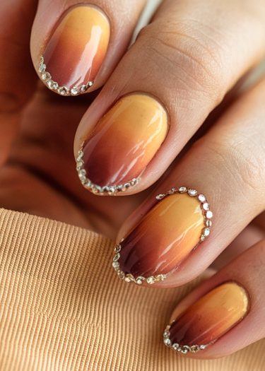 Elegant gradient sunset nails in golden yellow and burnt orange with sparkling rhinestones.