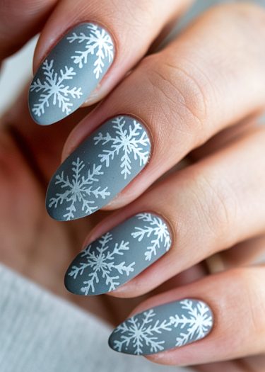 Elegant gray matte nails with intricate white snowflake designs for winter manicures.