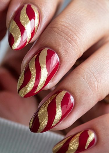 Elegant red and gold almond-shaped nail art with a glossy, wavy design.