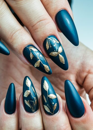 Elegant stiletto nails featuring deep teal matte polish with gold leaf designs.