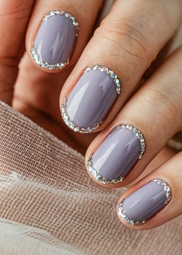 Elegant lavender nails with shimmering rhinestones on a textured background showcase exquisite nail art.