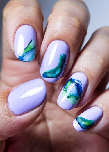 Elegant lavender nail art with unique watercolor designs in green and blue shades.