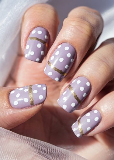 Elegant lavender nails featuring white polka dots and golden stripes for a chic manicure.