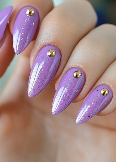 Elegant lavender stiletto nails adorned with gold beads for a sophisticated manicure.