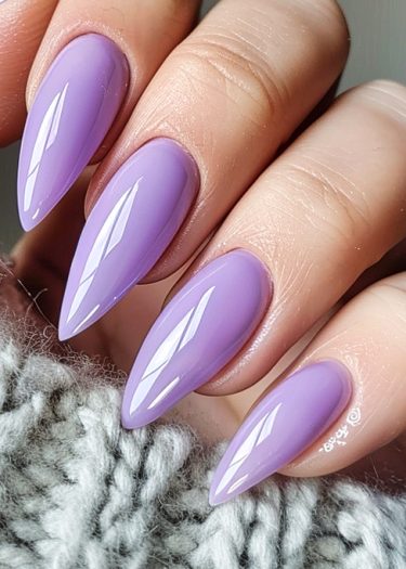 Elegant lilac stiletto nails complement cozy gray knitted fabric in a chic, stylish photo.