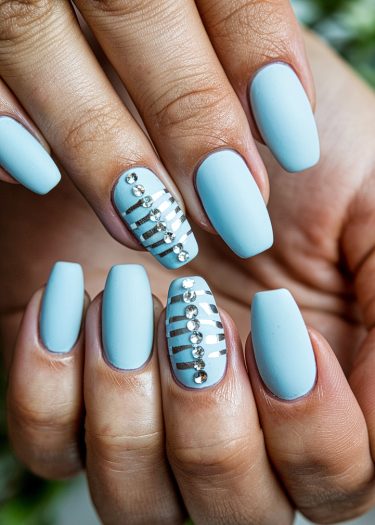 Elegant light blue matte nails with silver stripes and rhinestones for a trendy nail art design.