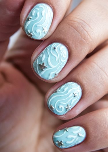 Elegant pastel blue nail art with white swirls and metallic star embellishments.