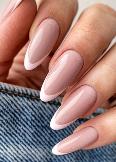 Elegant almond-shaped nails with light pink French tips against a stylish denim background.