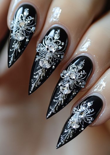 Elegant black stiletto nails adorned with sparkling crystal and silver filigree designs.