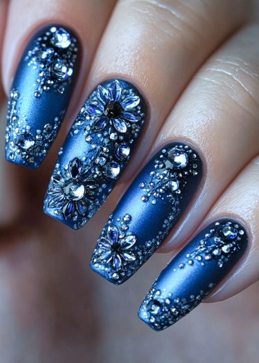 Luxurious navy blue matte nails adorned with sparkling crystals and floral designs for a glamorous look.