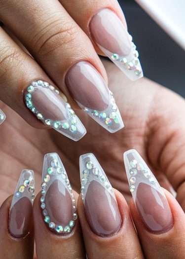 Elegant stiletto nail art with rhinestones and a nude glass-like finish for a sophisticated look.