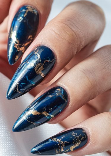 Luxury navy stiletto nails with intricate gold marbling, showcasing elegant nail art design.