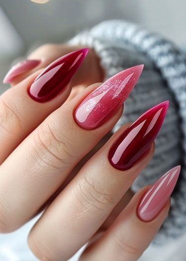 Elegant stiletto nails with gradient red and pink polish featuring glitter accents and glossy finish.