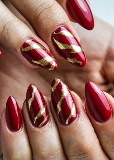 Elegant almond-shaped nails in deep red with gold designs showcase luxurious manicure artistry.