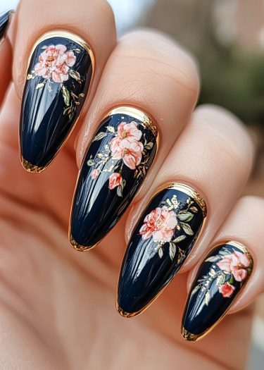 Elegant black almond-shaped nails featuring intricate floral designs and gold accents.