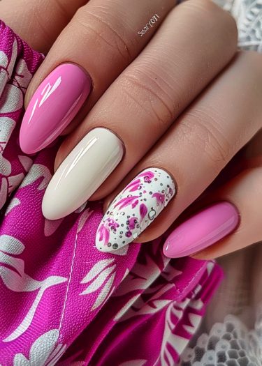 Beautifully manicured almond nails with pink and white designs on floral pink fabric.