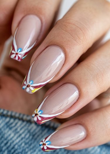 Elegant almond-shaped nude nails with vibrant floral designs and glossy finish on denim background.