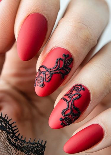 Elegant matte red almond nails with black lace design and well-groomed fingers.