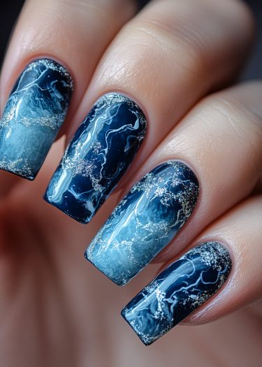 Elegant blue marbled nail art with sparkling accents and trendy coffin shape.