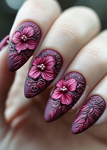 Elegant burgundy stiletto nails featuring intricate 3D floral nail art design with silver accents.