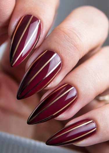 Elegant burgundy nails with gold stripes showcasing sophisticated nail art design.