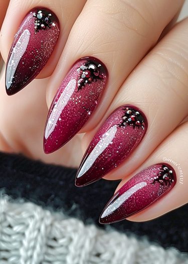 Stunning maroon ombre stiletto nails with glitter and pearl embellishments for a luxurious look.