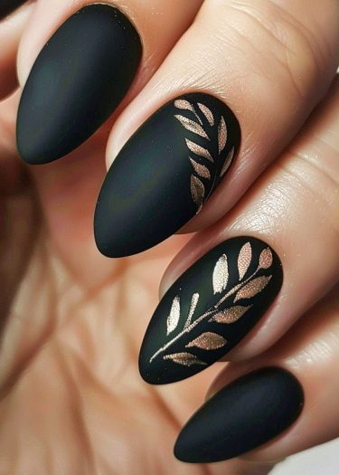 Elegant matte black almond nails featuring intricate gold leaf designs for a sophisticated look.