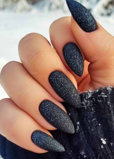 Elegant matte black glitter nails against a wintry backdrop and cozy attire.