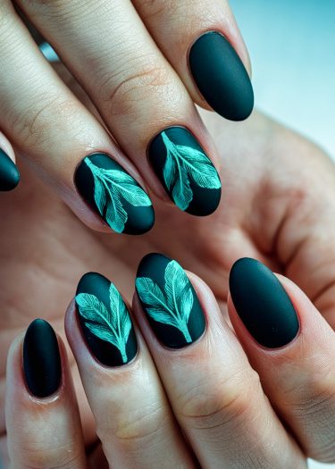 Matte black nails feature elegant leaf designs in turquoise-green for a sophisticated look.