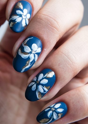 Intricate matte blue floral nail art with gold accents for elegant manicures.