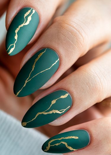 Elegant almond-shaped nails with matte emerald green polish and striking gold accents.