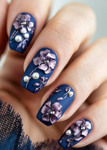 Elegant matte navy blue nail art with metallic floral designs and silver accents.