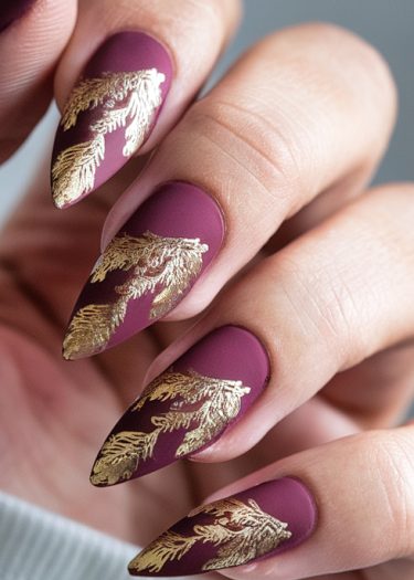 Elegant matte burgundy nails with intricate gold leaf designs for a luxurious manicure.