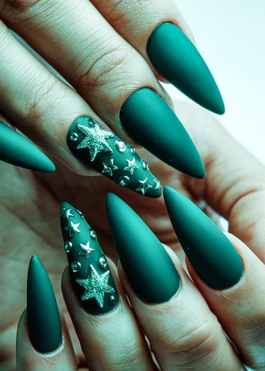 Striking matte teal stiletto nails adorned with silver stars and beads for a bold look.