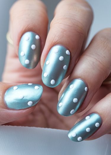 Stylish metallic blue manicure with white polka dots on elegantly shaped nails.