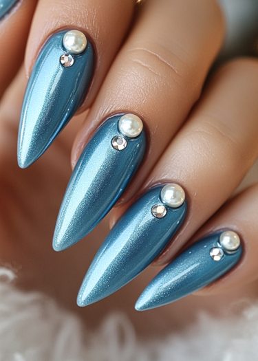 Elegant metallic blue stiletto nails with pearls and rhinestones for a striking manicure look.