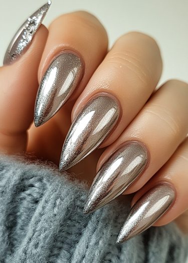 Stunning metallic chrome stiletto nails with glitter accents and a cozy sweater background.