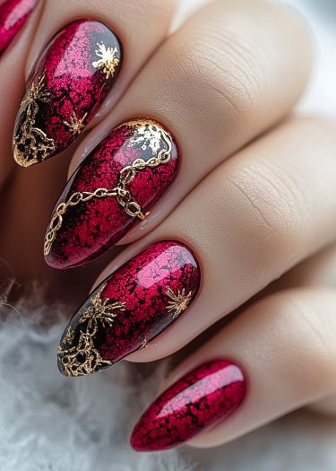 Elegant almond-shaped nail art featuring red polish, black marbling, and gold embellishments.