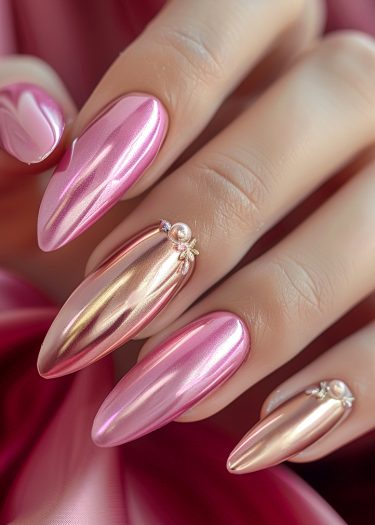 Elegant metallic pink almond-shaped nails with decorative accents on a soft pink fabric background.