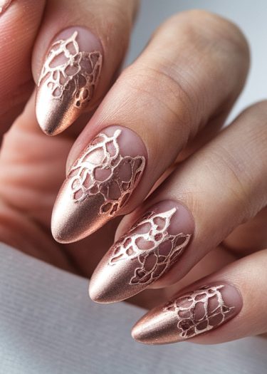 Elegant metallic rose gold almond nails with intricate lace designs and matte finish.