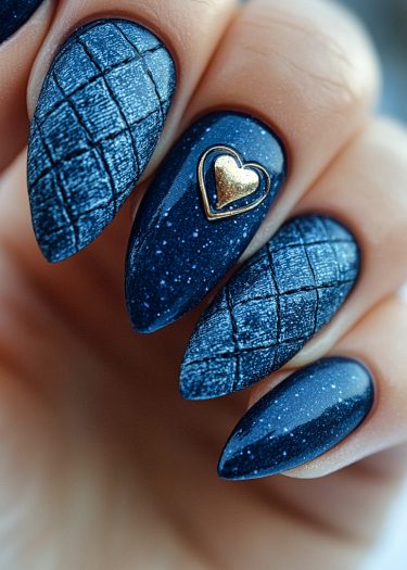 Elegant midnight blue nails with quilted texture and gold heart charm, showcasing nail artistry.