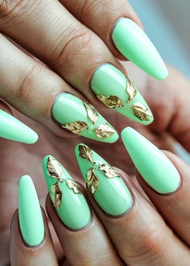 Elegant mint green almond nails adorned with gold leaf accents, showcasing modern nail art sophistication.