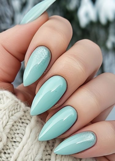 Elegant stiletto mint green manicure with glitter accents against a cozy knit background.