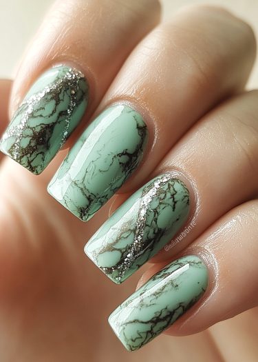 Elegant mint green marble nails with glitter accents showcase intricate nail art design.