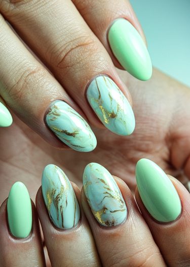 Elegant mint green marble nails with gold accents in a chic almond shape design.