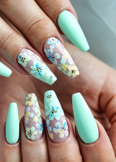 Artistic mint green nail design with floral patterns on almond-shaped tips.