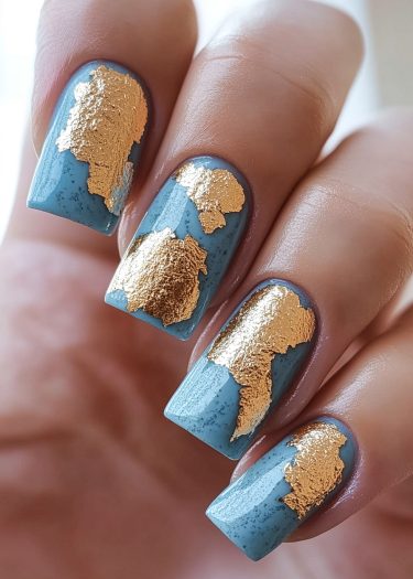 Stylish muted blue nails adorned with intricate gold foil designs for a luxurious look.