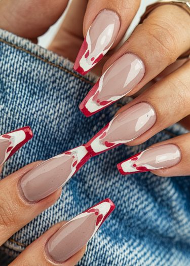 Elegant nude nails with vibrant red tips and artistic design on textured denim background.